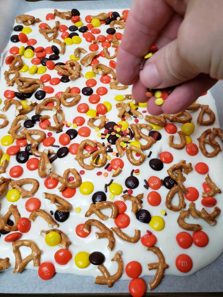 sprinkling pretzels and M&M's onto bark