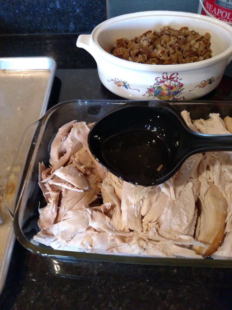 pouring broth over meat in baking dish and stuffing in another dish behind it