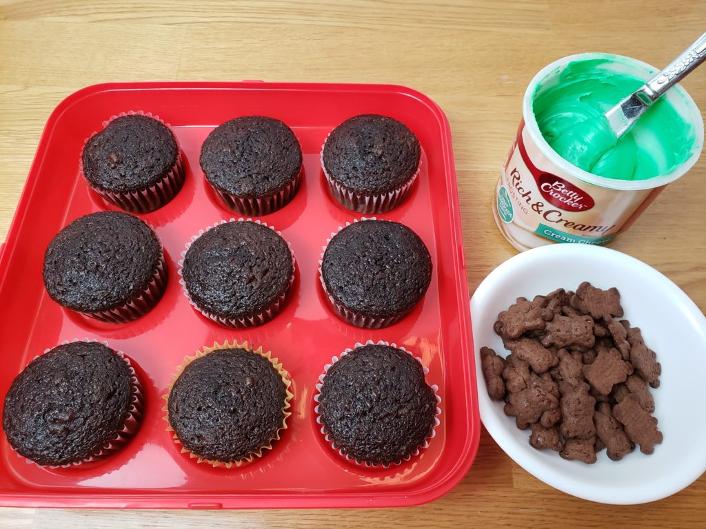 chocolate cupcakes, green icing and Teddy graham crackers in a bowl