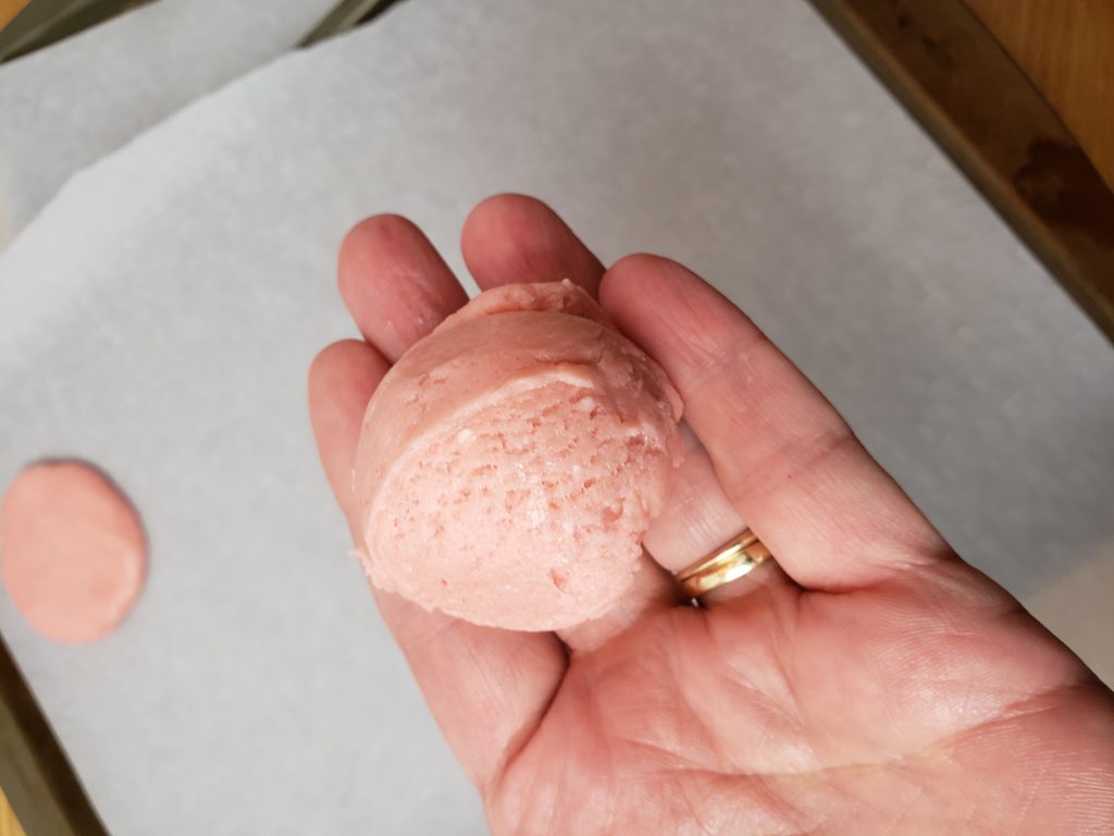 pink cookie dough in palm of hand showing size of ball to make