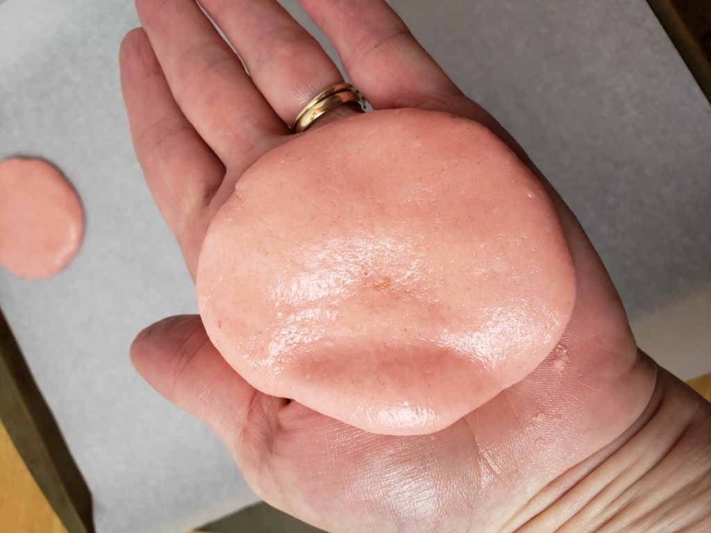 pink cookie dough in palm of hand showing how to flatten