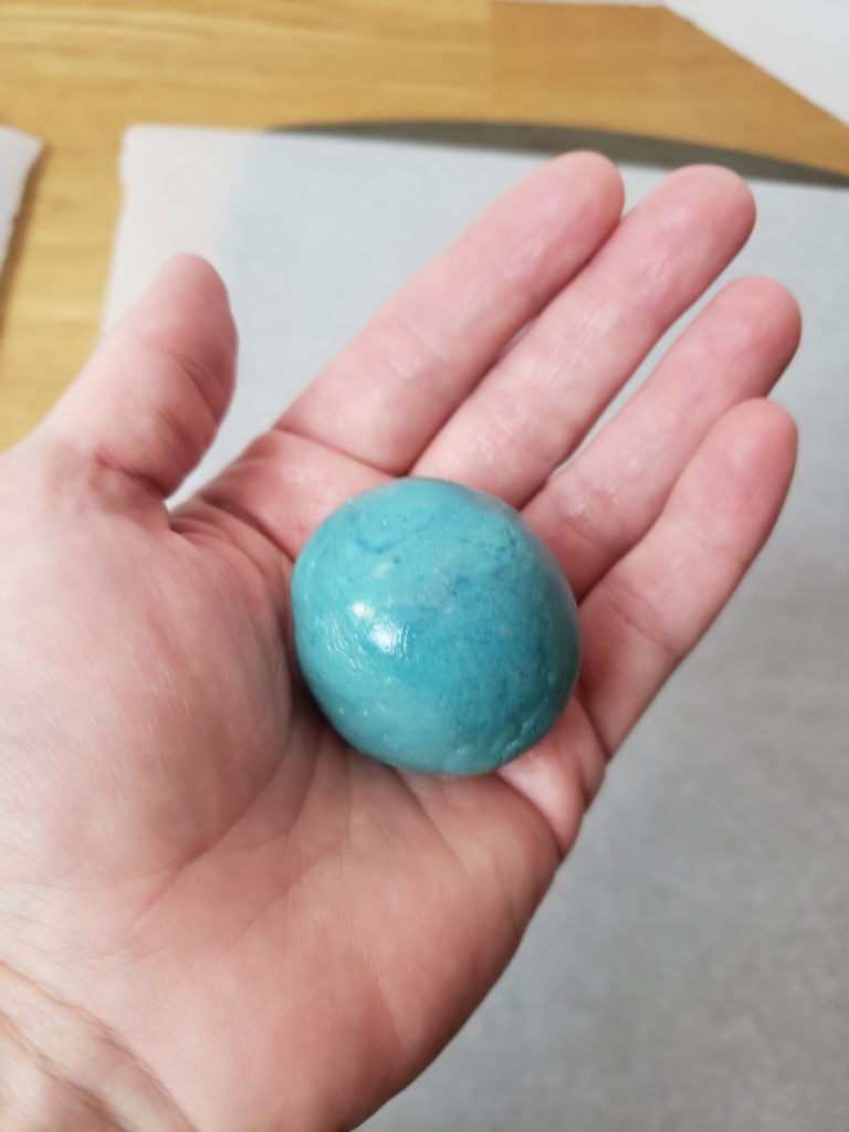 blue ball of unbaked cookie dough in hand