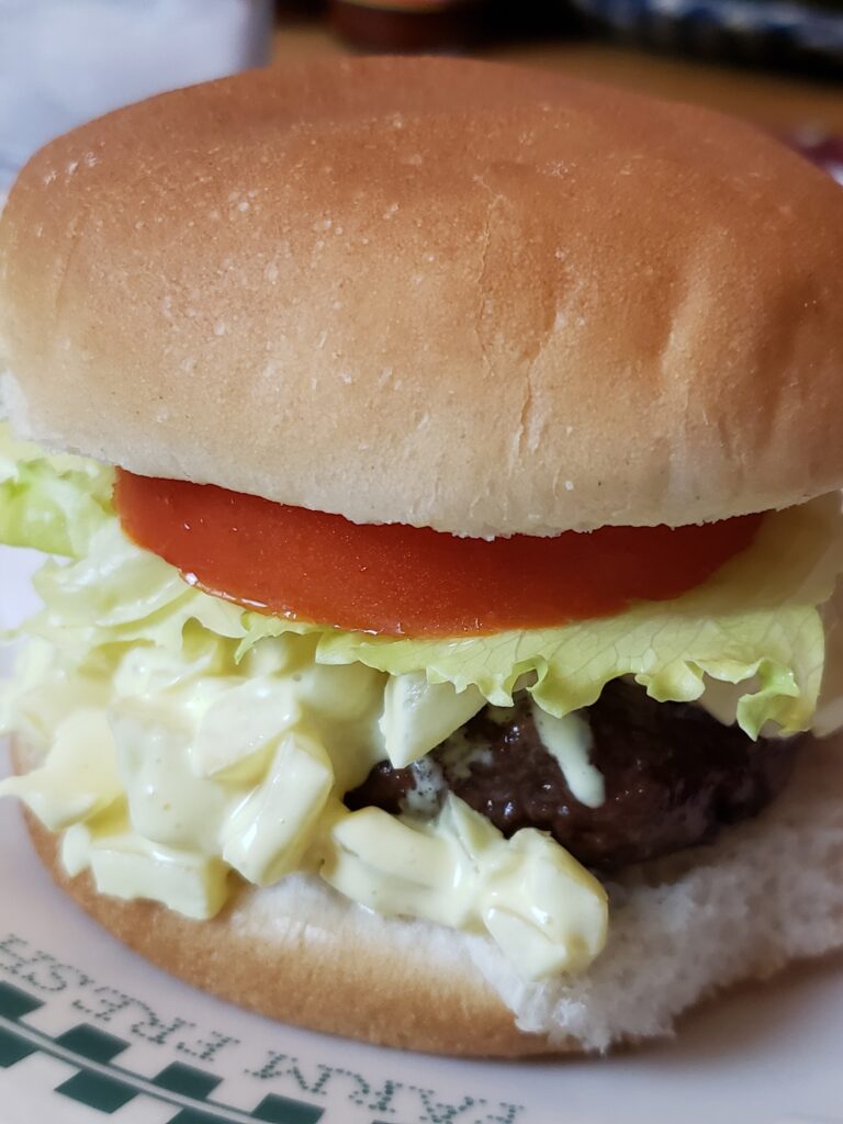 A hamburger with onion relish, tomato slice and lettuce.