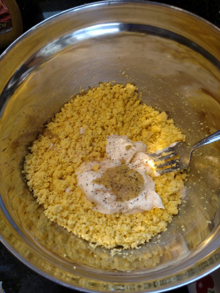 mayonnaise, mustard and seasonings added to mashed egg yolks in bowl.