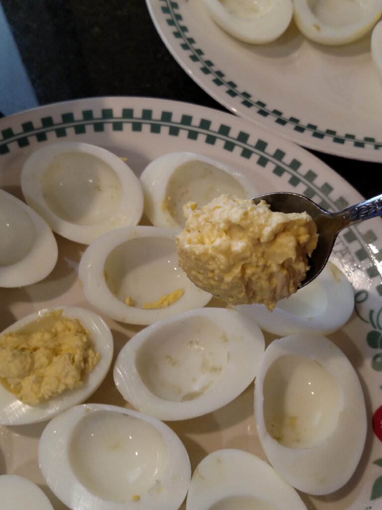 scooping deviled egg mixture back into white of eggs