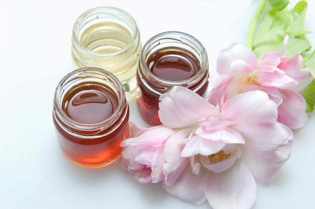 3 jars of honey of different colors and pink flowers on the side