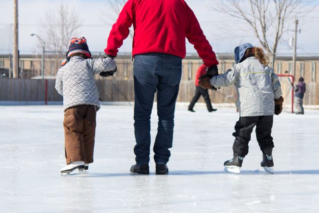 man ice skating and holding hands of 2 small children