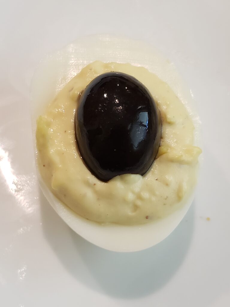 half of black olive on top of deviled egg as body of spider.