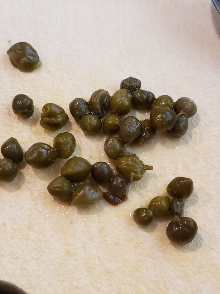 about 32 capers on a cutting board ready to be added to deviled egg.