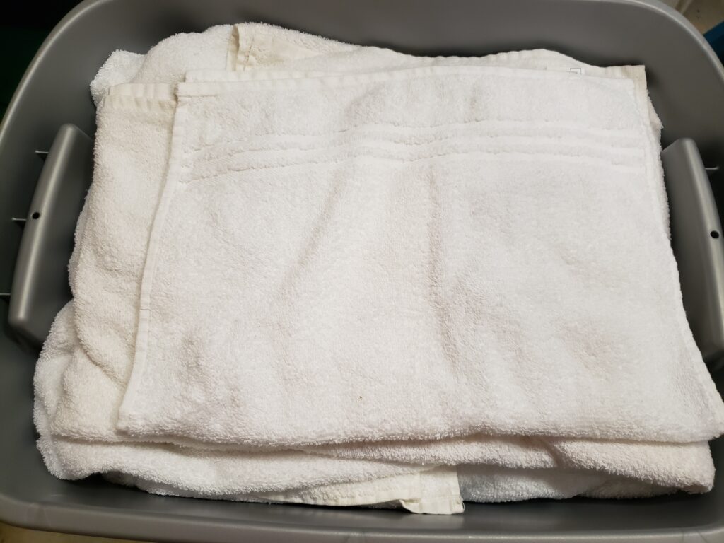 folded white towels in gray bin with cords wrapped in them