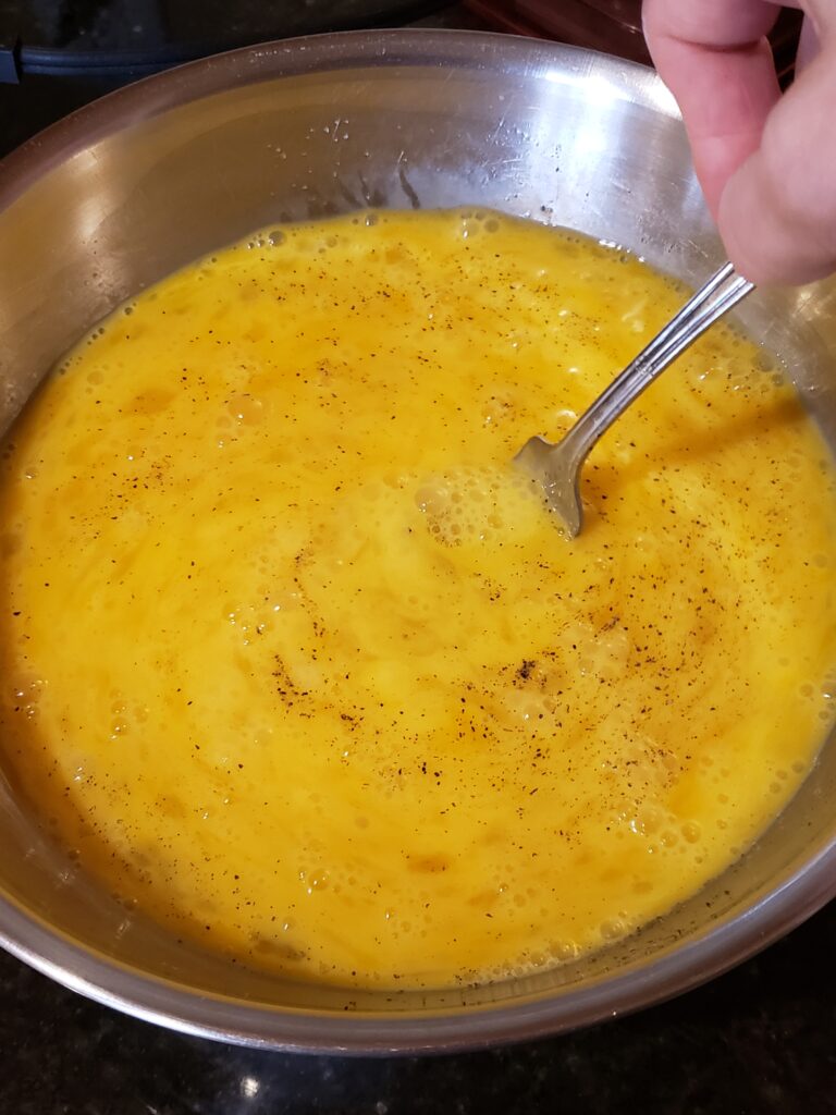 scrambling eggs in metal bowl with fork