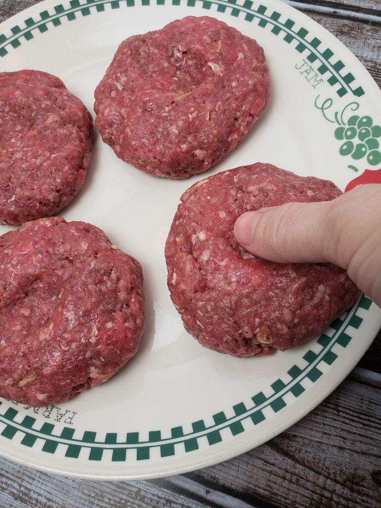 pressing an indent on a raw hamburger patty with thumb