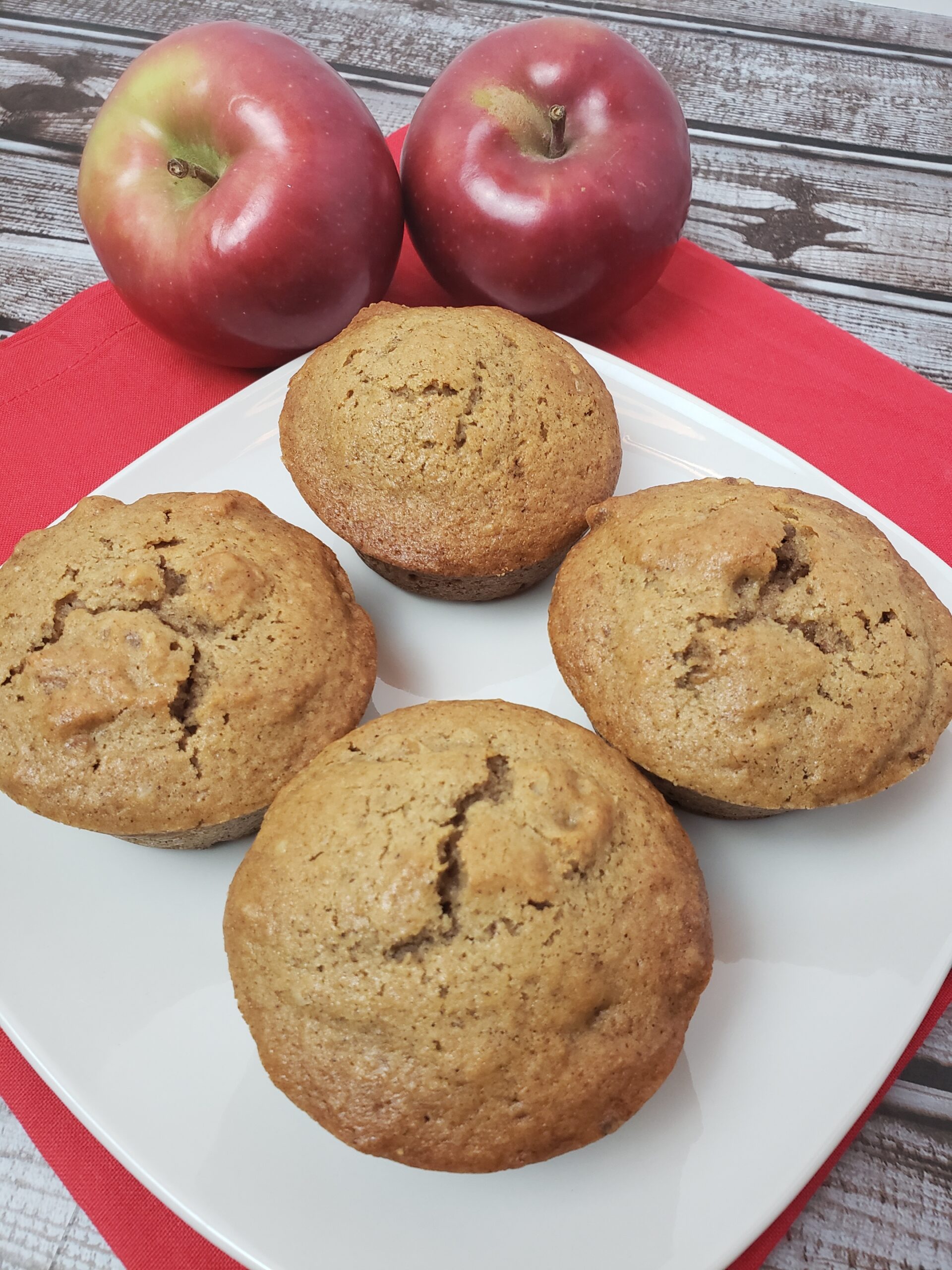 4 Easy Applesauce Muffins on a white plate with 2 apples next to them.