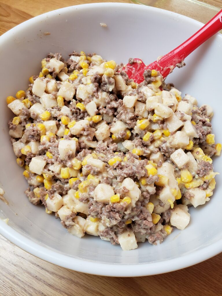 meat, cream of chicken soup, potatoes and corn mixed together in bowl