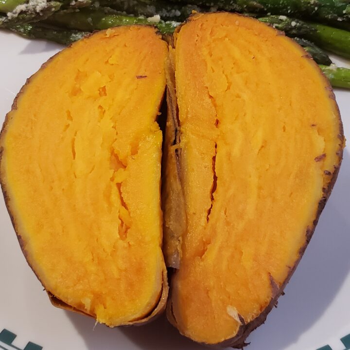 a big, orange, cooked sweet potato cut in half on a plate.