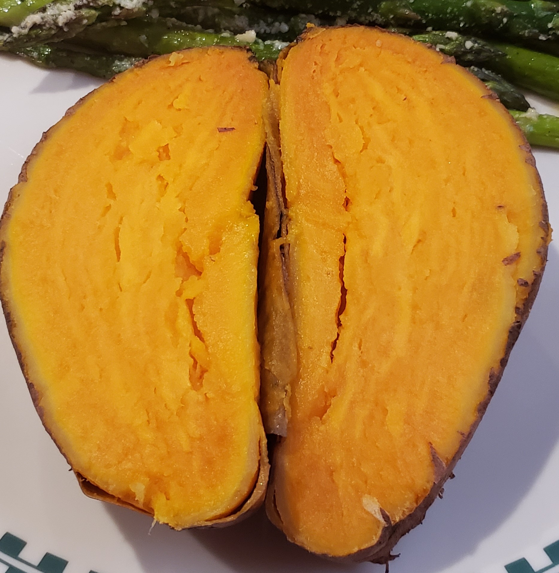 a big, orange, cooked sweet potato cut in half on a plate.