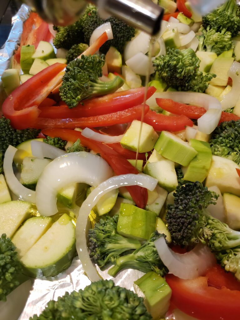 drizzling oil over vegetables on baking sheet