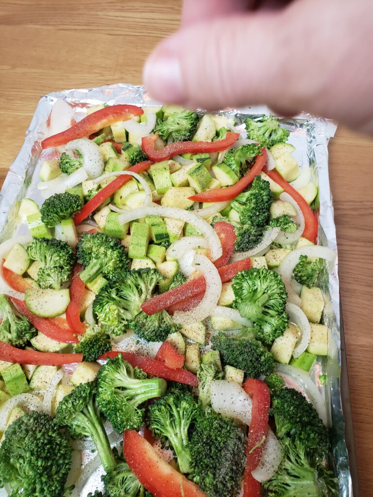 sprinkling spices on vegetables on baking sheet