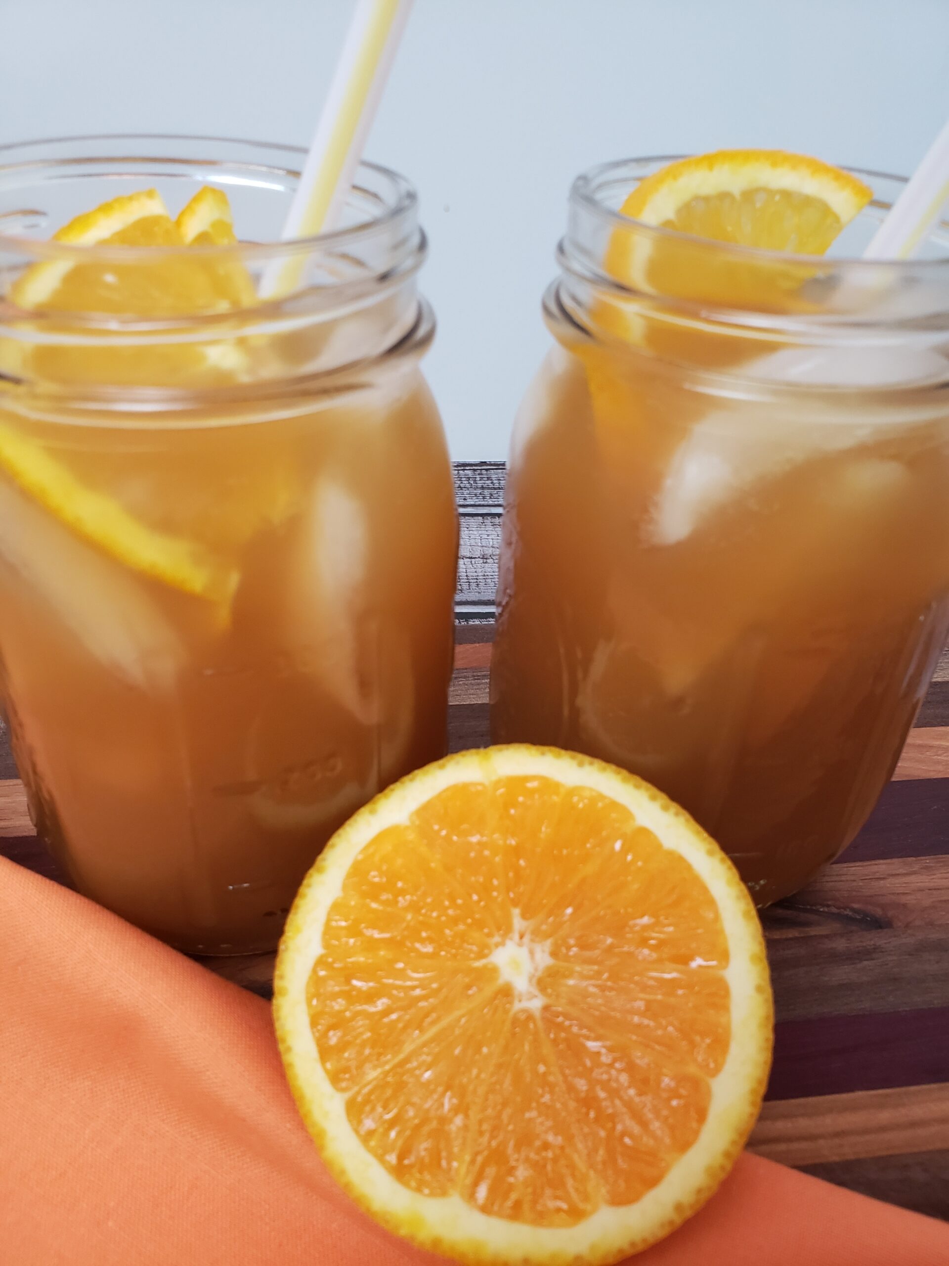 2 mason jars of orange honey iced tea and half of an orange in front of them.
