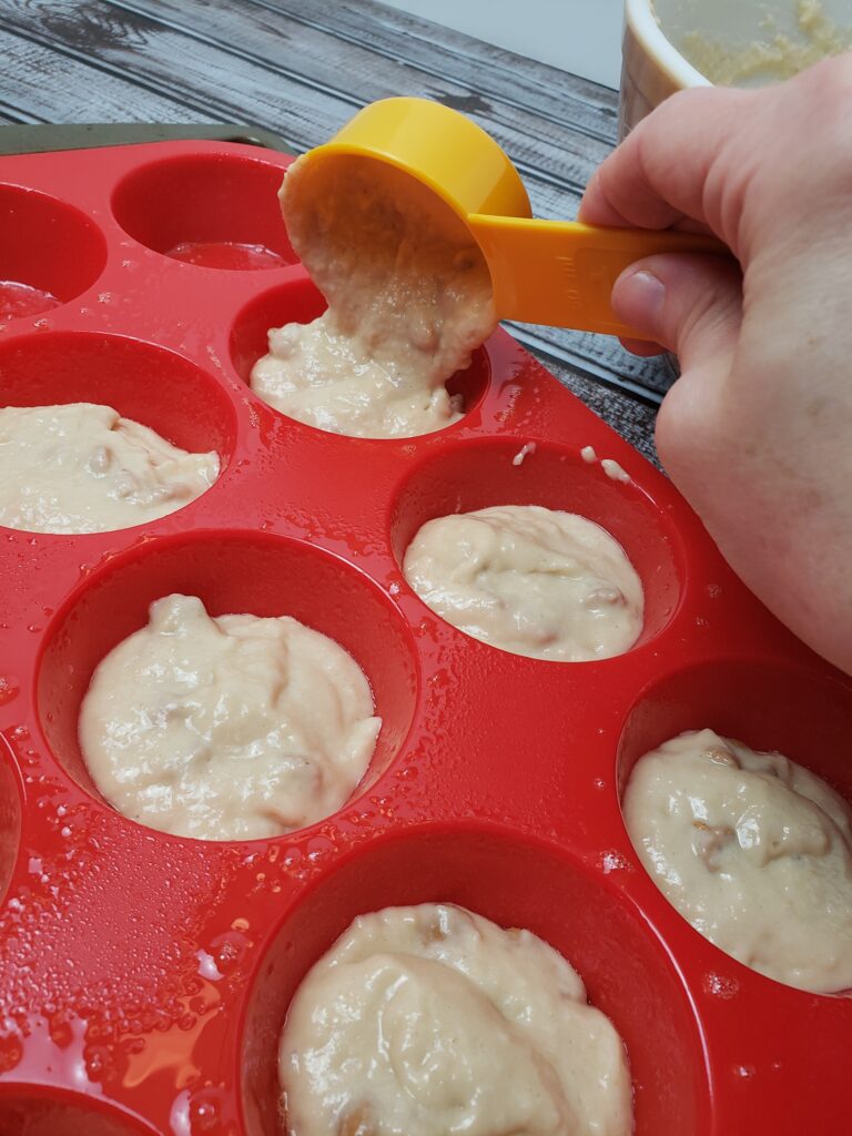 scooping muffin batter into muffin tray with measuring cup.