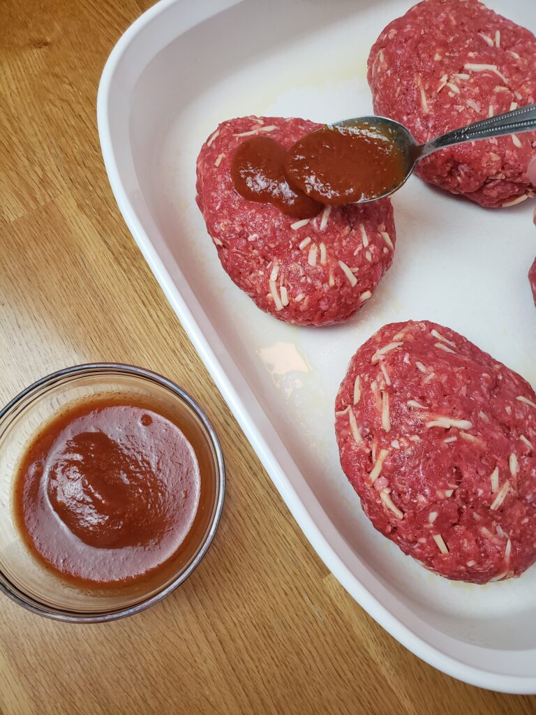 adding spaghetti sauce to the top of a meatloaf with a spoon