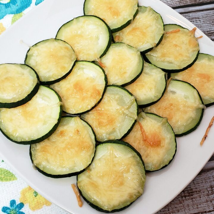 Cheesy Zucchini Coins on white plate next to kitchen towel with flowers