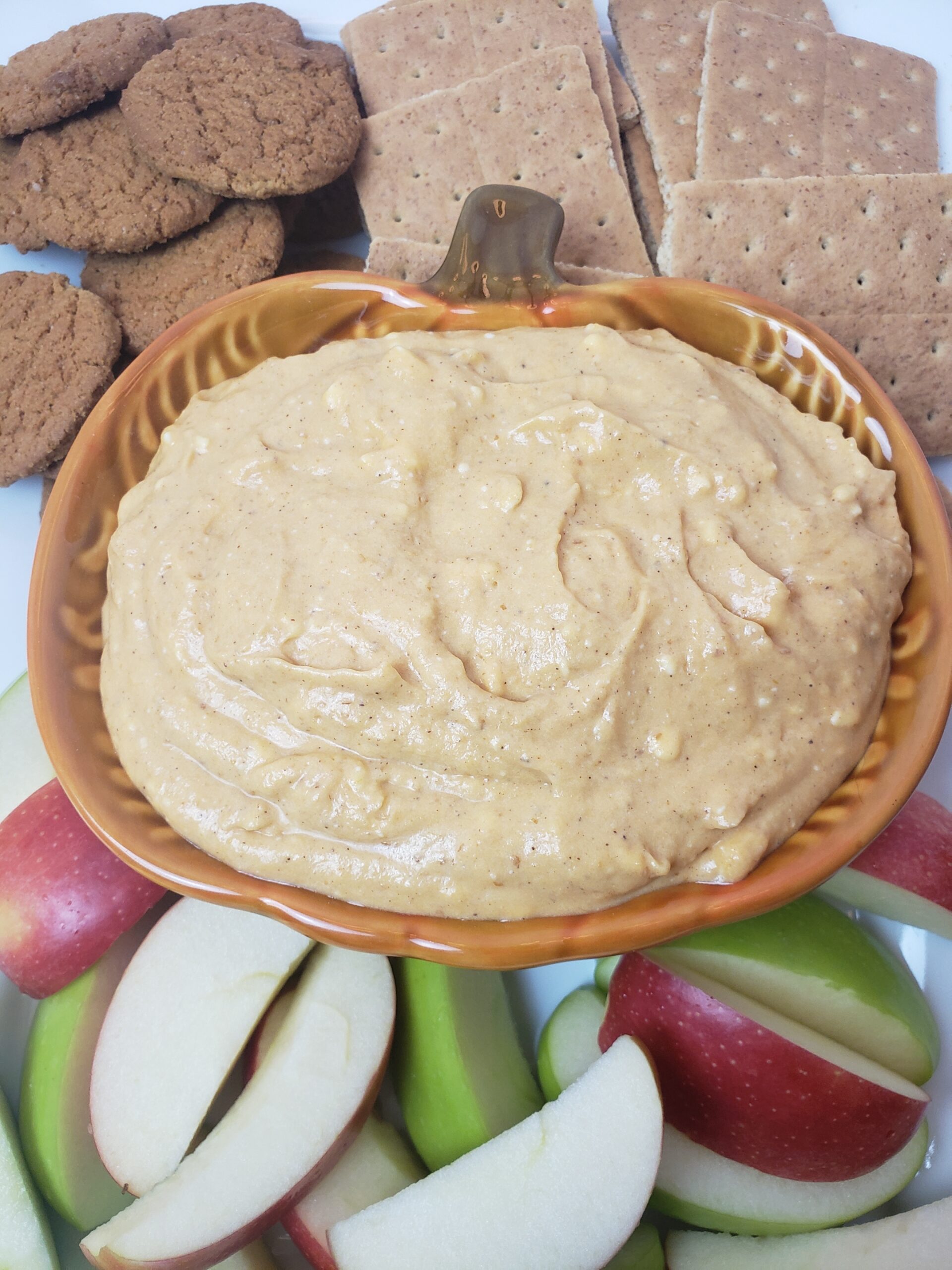 pumpkin dip served in pumpkin shaped bowl with ginger snaps, graham crackers and red and green apples.