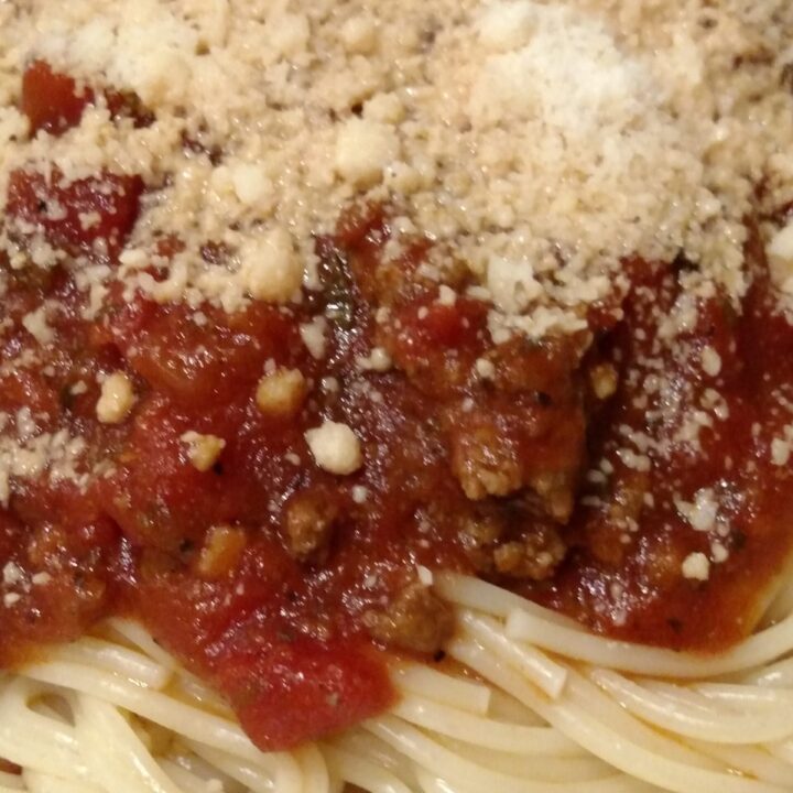 a pile of spaghetti noodles with meaty pasta sauce and cheese on top