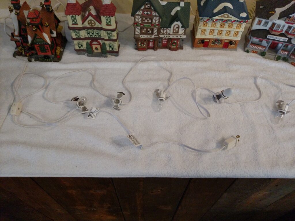 5 Christmas village houses with cord with 5 bulbs laid out in front of them