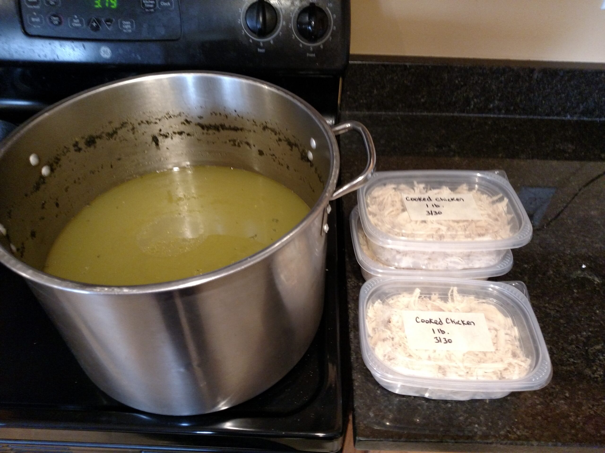 large pot on stove of chicken broth and three containers next to it of shredded chicken.