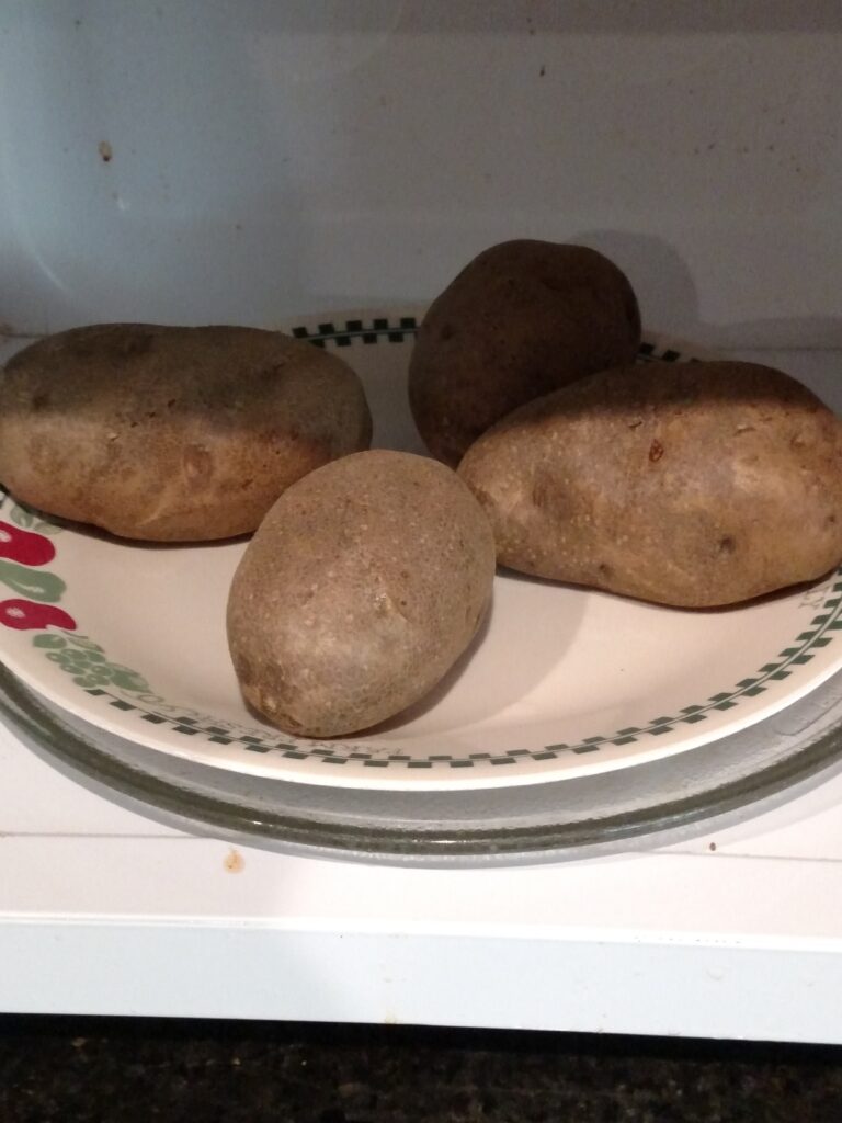 4 potatoes on a plate in the microwave.