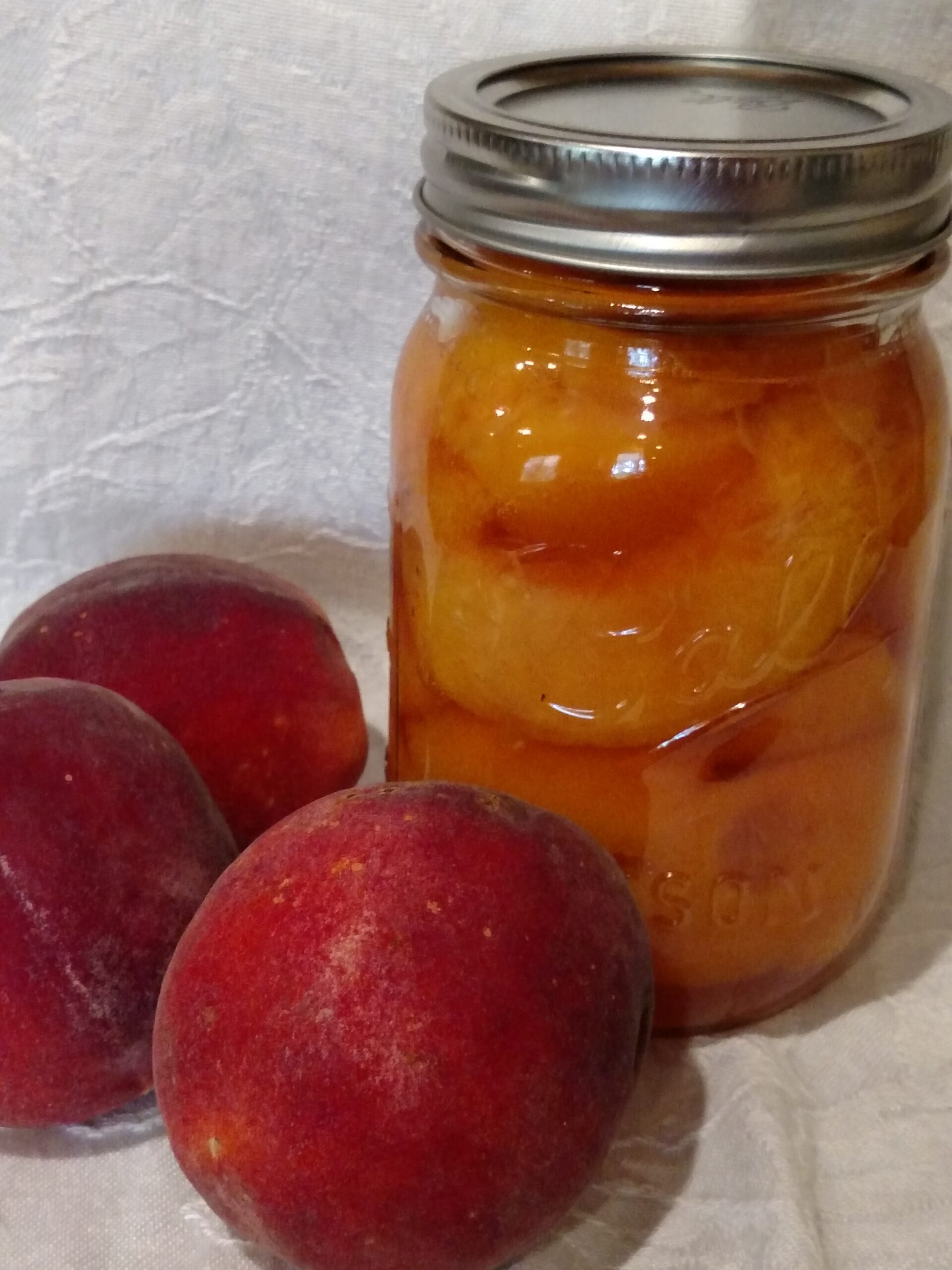1 pint jar of home canned peaches and 3 peaches next to it.