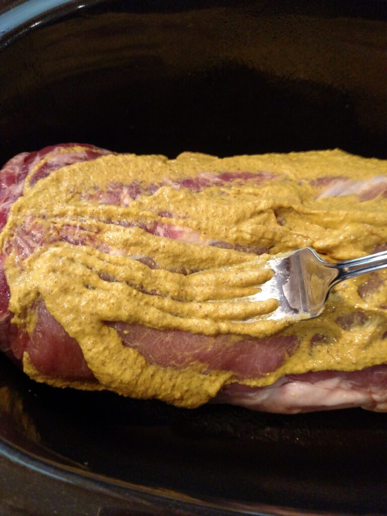 spreading mustard on pork with fork