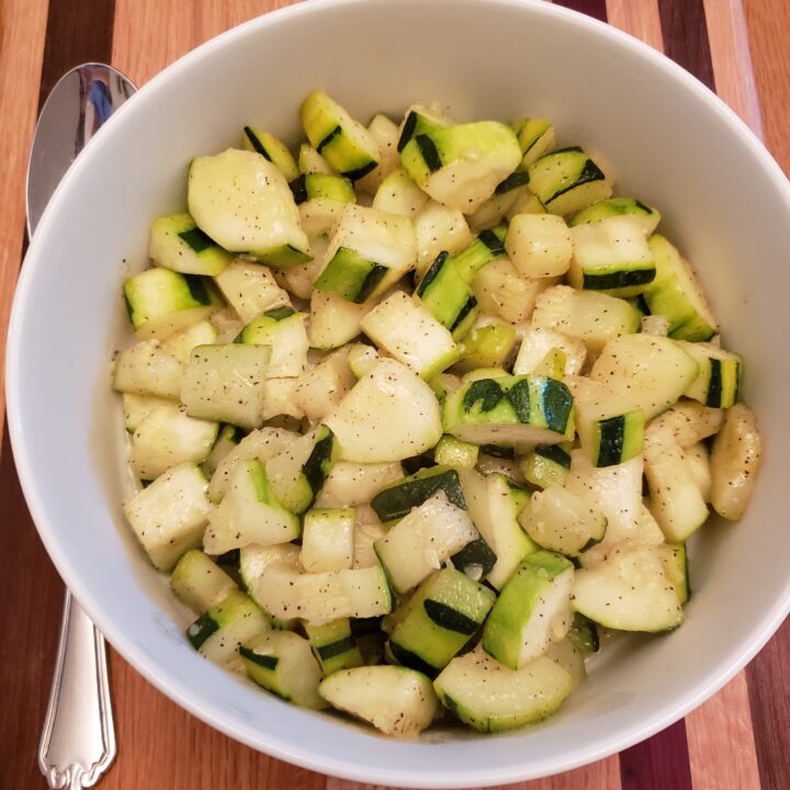 Simple Sautéed Squash in white bowl with serving spoon on the left.