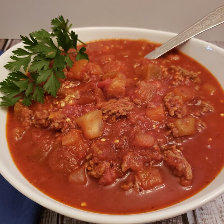 Instant Pot Eggplant Bolognese in white serving bowl with spoon and parsley for garnish.