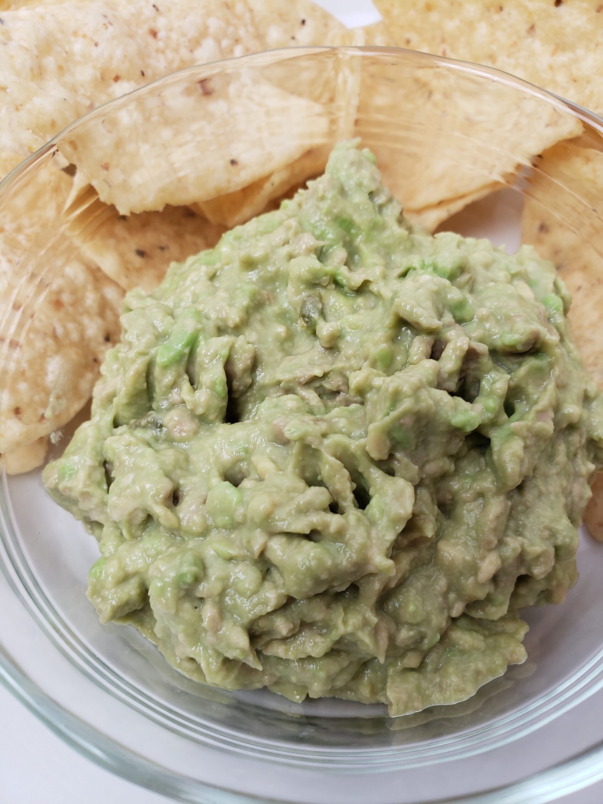 Simple Creamy Guacamole in glass dish surrounded by tortilla chips.
