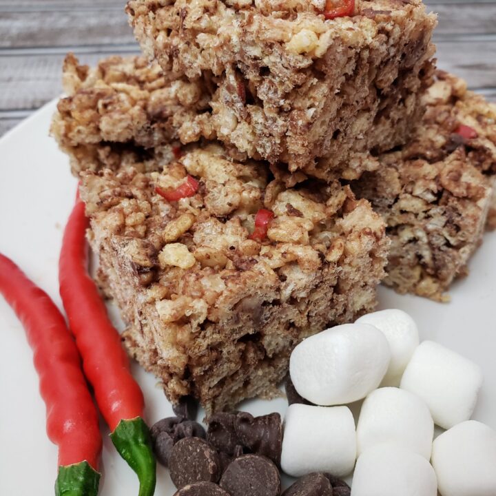 Chocolate Cayenne Rice Krispy Treats on plate with extra cayenne peppers, chocolate chips and mini marshmallows.