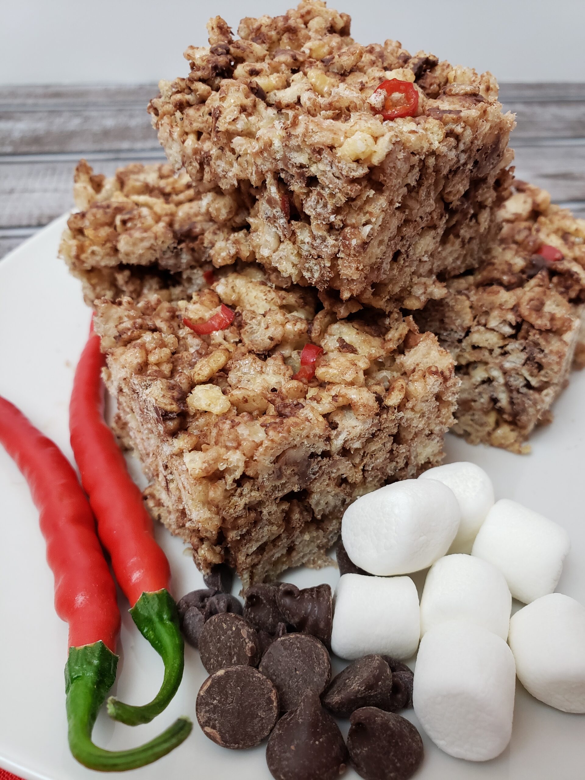 Chocolate Cayenne Rice Krispy Treats on plate with extra cayenne peppers, chocolate chips and mini marshmallows.