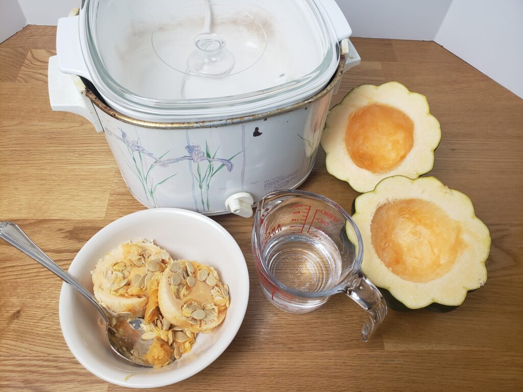 acorn squash cut in half, cup of water, bowl with seeds in it and slow cooker