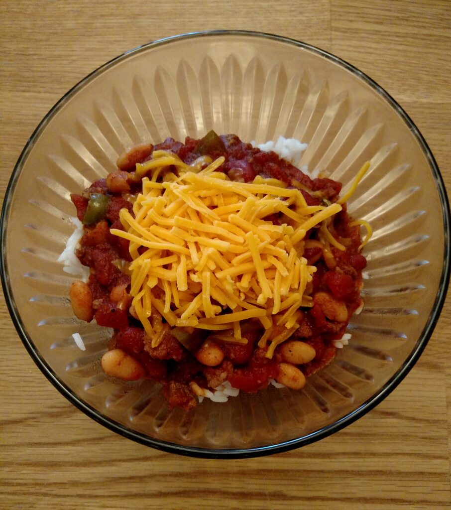 big batch homemade chili in serving bowl over rice and with shredded cheese on top