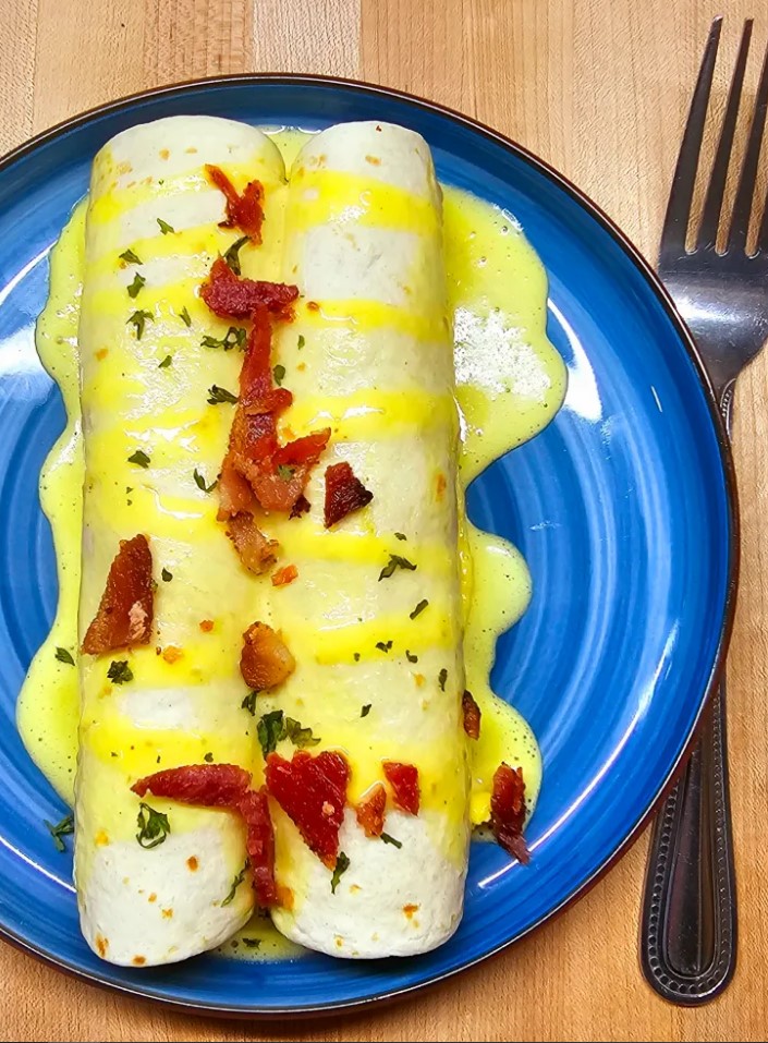 2 hollandaise breakfast enchiladas on a blue plate