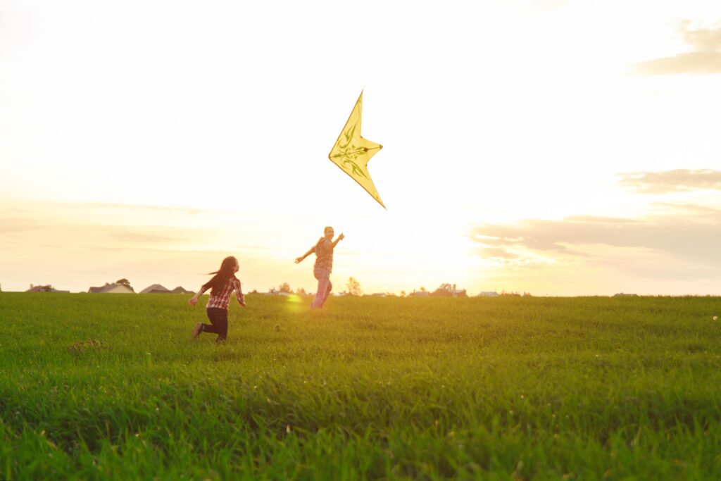 man and girl running in a field of grass with a yellow kite