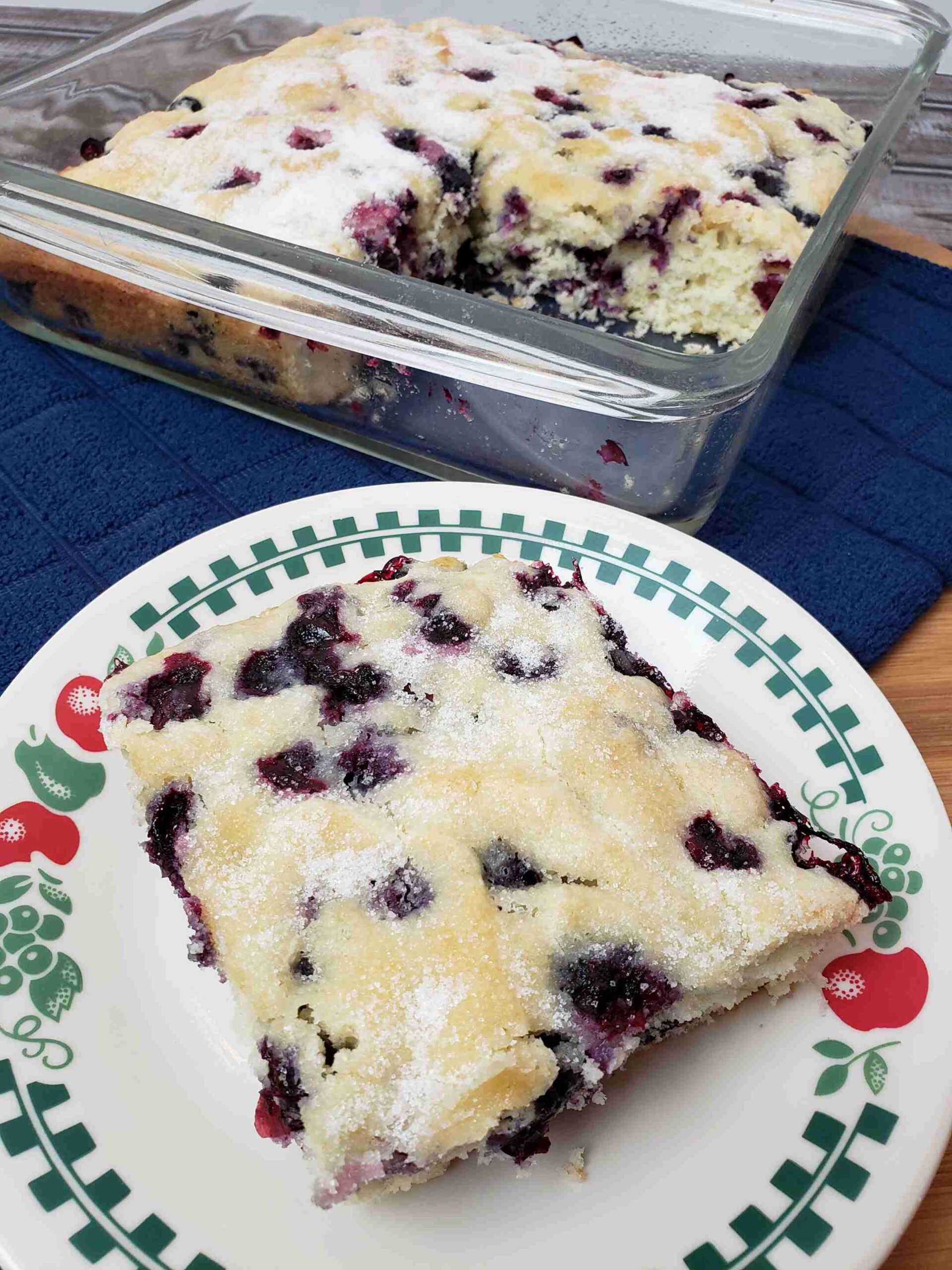 Overnight Blueberry Coffee Cake with a piece on plate in front of baking dish