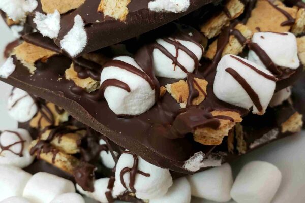 s'mores bark broken and stacked on a white plate with mini marshmallows in front of it.