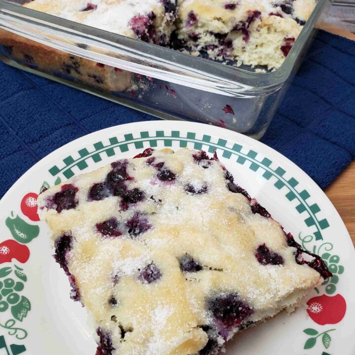 Overnight Blueberry Coffee Cake with a piece on plate in front of baking dish