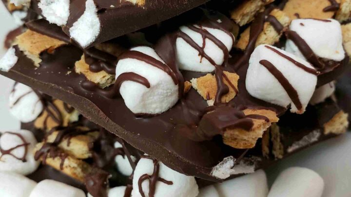 s'mores bark broken and stacked on a white plate with mini marshmallows in front of it.
