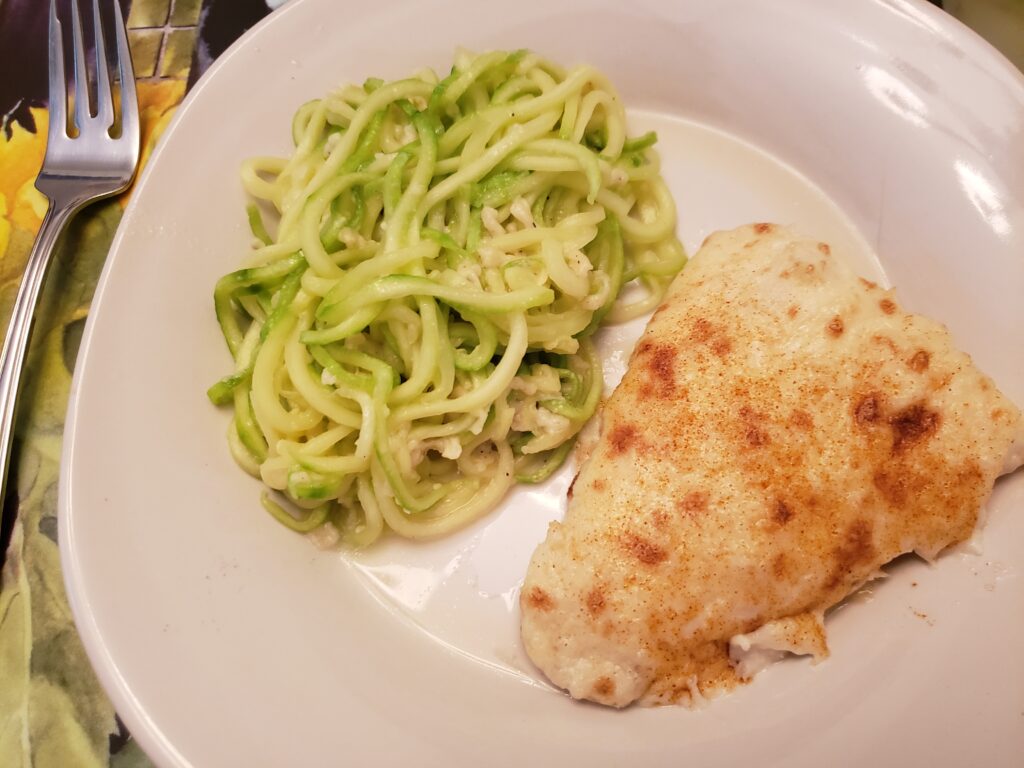 crab topped fish and zucchini noodles parmesan on a white plate