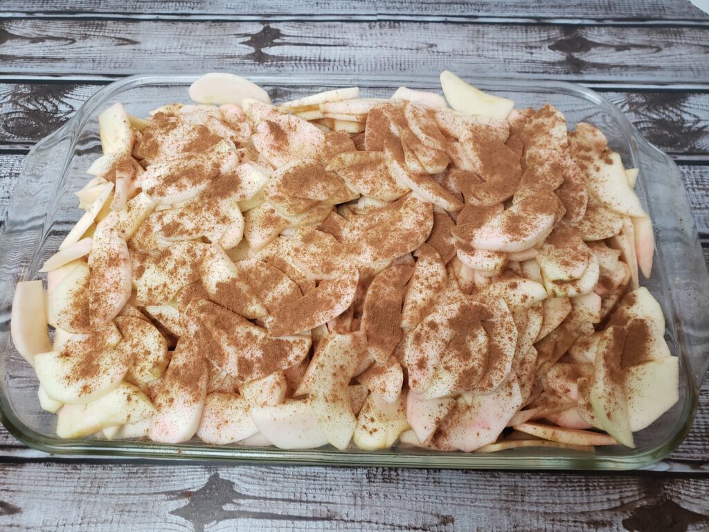 sliced apples piled high in baking pan with cinnamon on top