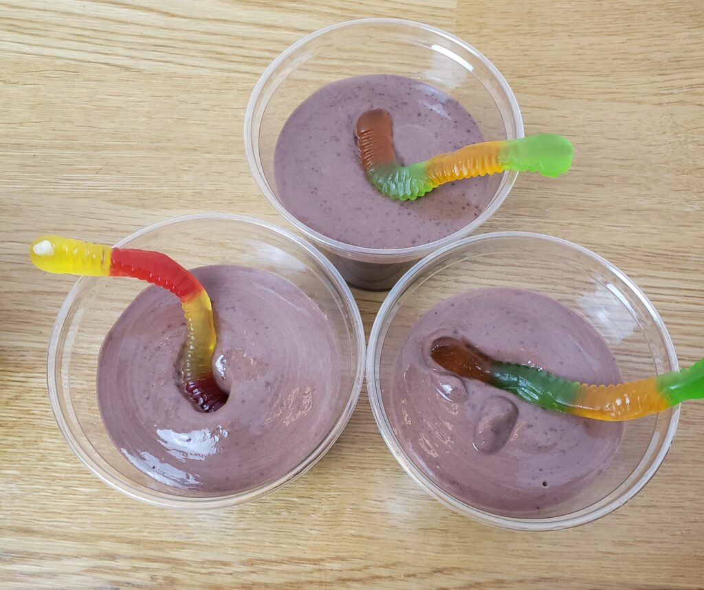 chocolate pudding in 3 plastic cups with 1 gummy worm each