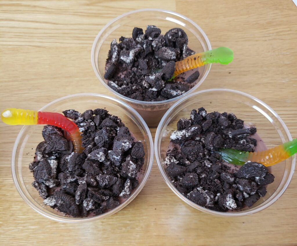 chocolate pudding in 3 plastic cups with 1 gummy worm each and crushed Oreos on top